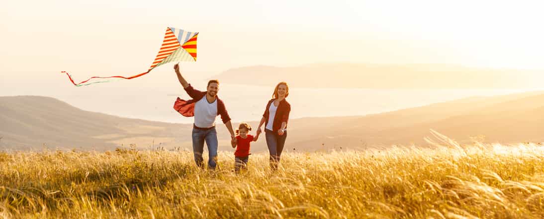 Family Running Through Field with Kite